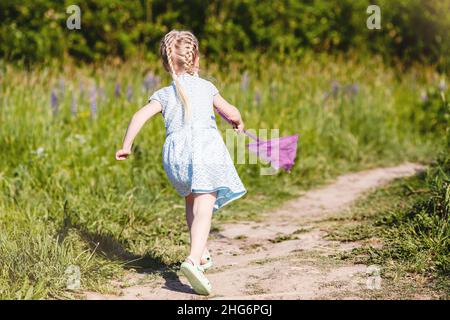 La petite fille est ronnig sur le chemin de la forêt pour attraper le papillon avec le filet Banque D'Images