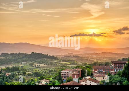 Coucher de soleil dans le petit village de Chiusi Toscane Italie avec maisons toits sur la campagne vallonnée paysage de collines et couleur jaune orange Banque D'Images