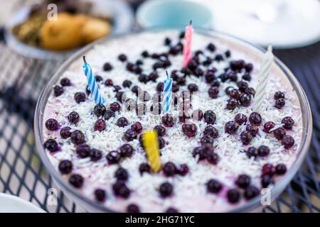 Macro gros plan de petit gâteau au fromage bleu-bleuet maison dessert gâteau végétalien cru dans un bol en verre avec bougies d'anniversaire colorées sur la table et la merde Banque D'Images