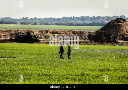 Gaza, Palestine.18th janvier 2022.Les agriculteurs travaillent sur une ferme près de la clôture séparant Gaza et Israël, tandis que les véhicules militaires israéliens tordent des parties de terres agricoles palestiniennes à Khuza'a, à l'est de Khan Yunis, dans le sud de la bande de Gaza.Crédit : SOPA Images Limited/Alamy Live News Banque D'Images