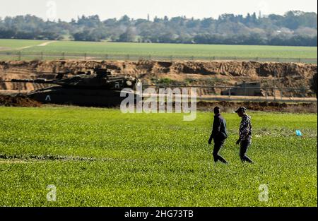 Gaza, Palestine.18th janvier 2022.Les agriculteurs travaillent sur une ferme près de la clôture séparant Gaza et Israël, tandis que les véhicules militaires israéliens tordent des parties de terres agricoles palestiniennes à Khuza'a, à l'est de Khan Yunis, dans le sud de la bande de Gaza.Crédit : SOPA Images Limited/Alamy Live News Banque D'Images