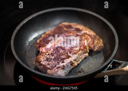 Gros plan de la croûte marron charrée sur les côtes de ribeye rares à base d'herbe cuisson du steak sur une poêle à frire antiadhésive avec assaisonnement au sel de poivre Banque D'Images