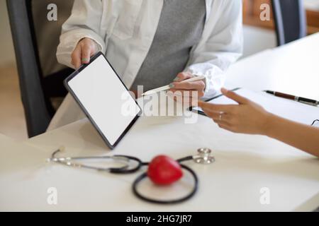 Image rapprochée d'un médecin ou d'un thérapeute montrant des informations sur sa tablette numérique à sa patiente.Écran vide de la tablette. Banque D'Images