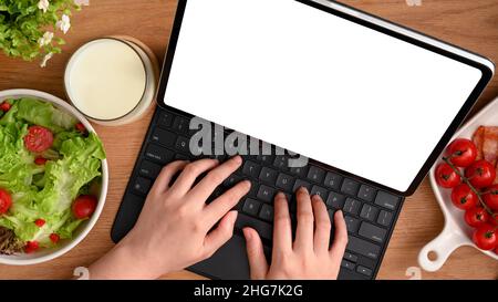 Une femme en bonne santé qui travaille sur sa tablette tout en prenant un petit déjeuner sain.Saladier et tomates fraîches sur la table. Vue de dessus Banque D'Images