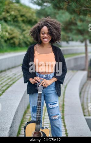 Femme à la peau sombre souriant à la caméra debout avec guitare Banque D'Images