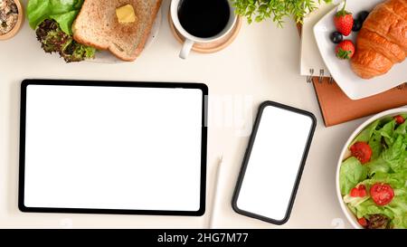 Un écran vide de smartphone et de tablette se présente sur un fond de table blanc entouré d'aliments sains. Banque D'Images