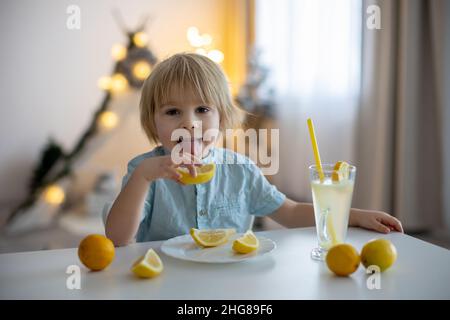 Mignon petit enfant, blond garçon, lécher des citrons à la maison et boire de la limonade, faire des visages drôles Banque D'Images