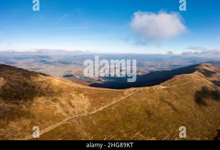 De longues allées étroites longeant la crête de haute montagne sous des nuages blancs moelleux flottant sur le ciel bleu sur une vue aérienne de jour ensoleillé Banque D'Images