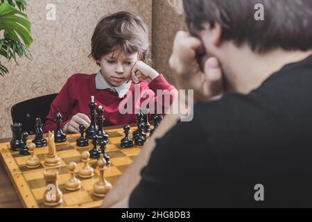 Un garçon de six ans qui réfléchit à jouer aux échecs avec son père qui réfléchit à faire bouger.Activités de loisirs pendant la quarantaine Banque D'Images