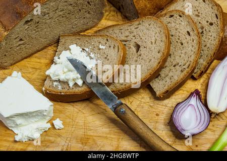 Pain fait maison sur une planche à découper en bois avec du fromage caillé.Décoration avec des oignons verts frais ou des ciboules. Banque D'Images