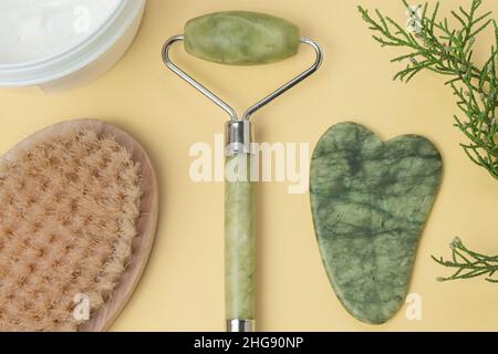 Flatlay avec crème, rouleau de visage, visage gua sha, pinceau de massage sur fond jaune. Concept spa et soin naturel de la peau Banque D'Images