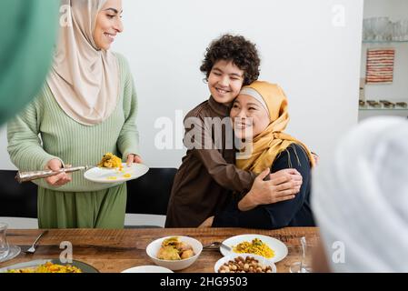 Un garçon musulman souriant embrassant une grand-mère asiatique près d'une mère et se nourrgeant à la maison Banque D'Images