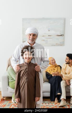 homme musulman d'âge moyen qui embrasse l'épaule du petit-fils arabe près d'une famille multiethnique sur un fond flou Banque D'Images