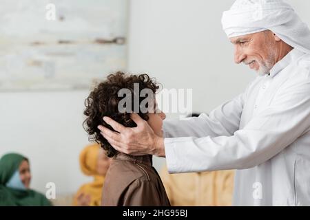 un homme musulman heureux en turban qui embrasse la tête du petit-fils arabe près d'une famille multiethnique floue Banque D'Images