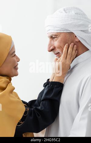 vue latérale d'une femme asiatique heureuse dans le hijab touchant le visage du mari musulman Banque D'Images