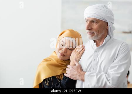 une femme asiatique heureuse d'âge moyen avec les yeux fermés penchée sur le mari musulman à la maison Banque D'Images