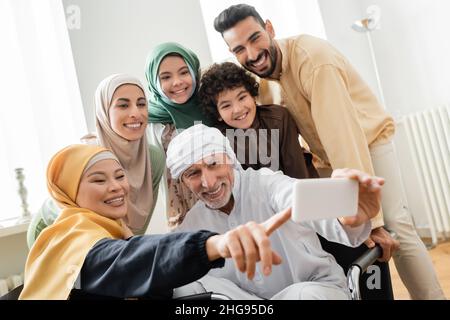 joyeuse femme asiatique pointant du doigt près d'un musulman prenant le selfie avec une famille interraciale Banque D'Images