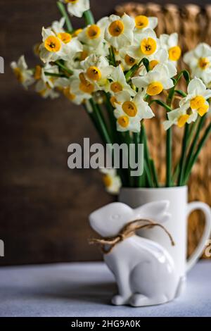 Décoration de lapin de Pâques à côté d'un bouquet de fleurs narcissus dans une carafe Banque D'Images