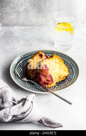 Tranche de gâteau éponge de myrtille et de cerise sur une assiette avec un verre d'eau de citron Banque D'Images