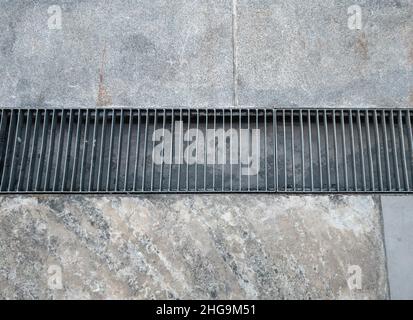 La grille métallique du canal de drainage près de la chaussée devant un centre commercial de la ville, vue de face avec l'espace de copie. Banque D'Images