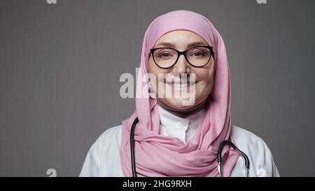 La jeune femme médecin dans hijab sourit largement regardant dans l'appareil photo Banque D'Images