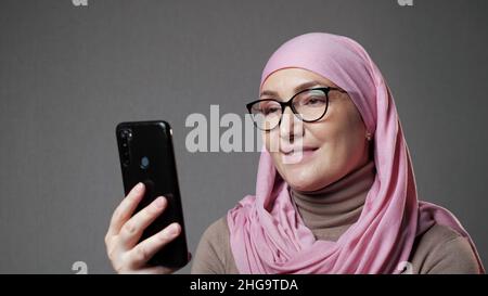 Une jeune femme musulmane en hijab sourit en regardant un spectacle au téléphone Banque D'Images