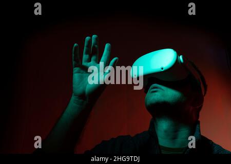 Homme avec des lunettes blanches de réalité virtuelle avec fond rouge levant la main Banque D'Images
