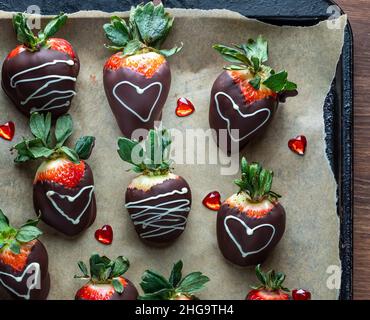 Fraises enrobées de chocolat décorées sur papier parchemin pour la Saint-Valentin. Banque D'Images