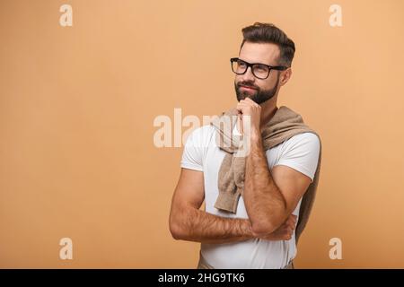 Portrait d'un homme beau et réfléchi barbu avec des lunettes noires dans un style décontracté de réflexion et de réflexion.Studio tourné sur fond orange Banque D'Images
