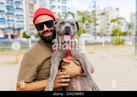 Joyeux homme de course mixte dans des lunettes jouant avec son chien dans le parc de sity Banque D'Images