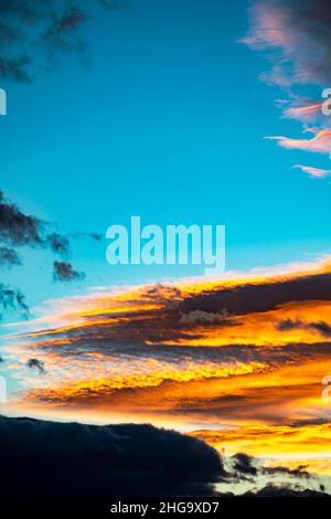 Une image portrait de nuages orange et jaune dorés dans un ciel bleu au coucher du soleil sur la côte méditerranéenne de Marbella Banque D'Images