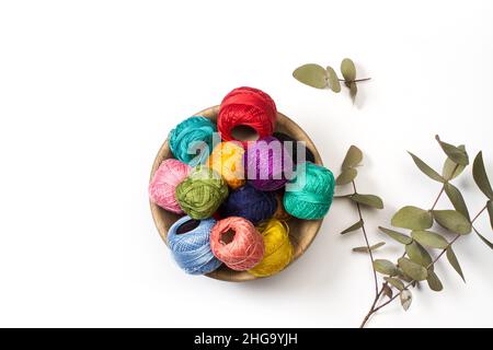 Bobines de fil de couleur dans un bol en bois sur fond blanc avec des leves d'eucalyptus Banque D'Images