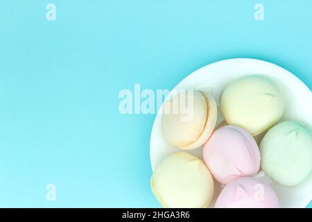 Les guimauves douces et aérées de couleur pastel et blanche ressemblent à des macarons posés sur une assiette, sur un fond pastel Banque D'Images