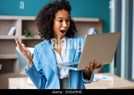 Belle femme d'affaires adulte avec robe élégante debout dans un studio d'affaires et utilisant ordinateur portable pour une vidéo conférence en ligne - African ameri Banque D'Images