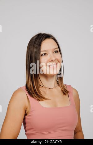 Portrait de brunette souriante.Belle jeune femme heureuse posant sur fond gris isolé en studio, elle porte le dessus beige pour le yoga ou la forme physique Banque D'Images