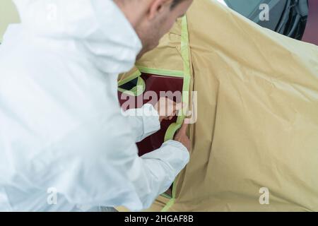 Vue rapprochée de l'auto-peintre qui masque un corps de voiture avant de peindre avec du ruban adhésif et du papier Banque D'Images