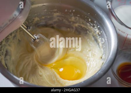 Faire un gâteau: Ajouter un oeuf et battre la pâte.Batteur montrant un flou de mouvement.Lait et vanille en arrière-plan. Banque D'Images