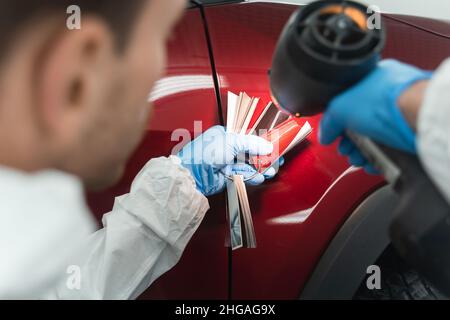 Auto peintre avec une lampe coloriste et des échantillons qui choisissent une nuance de peinture de voiture Banque D'Images