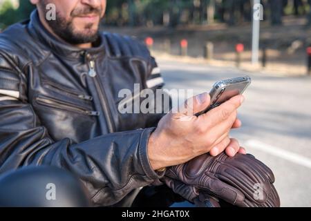 Un motard élégant utilisant un téléphone portable sur une route rurale. Banque D'Images