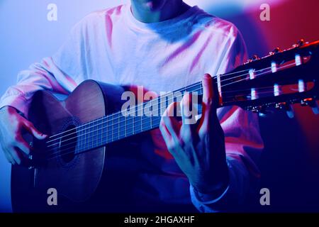 Gros plan des doigts sur le cou d'une guitare acoustique.Muchina joue la guitare au néon.Musicien, musique, formation. Banque D'Images