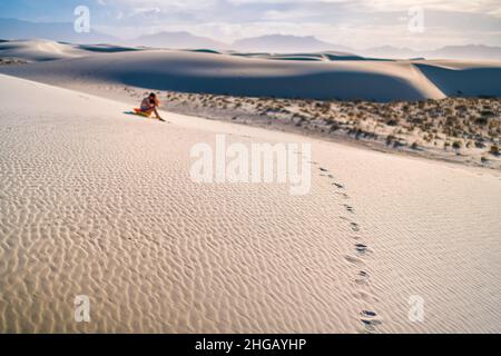 Jeune femme sur le célèbre monument national des dunes de sable blanc au Nouveau-Mexique assis sur un traîneau à disques pour glisser sur la colline pendant le coucher du soleil Banque D'Images