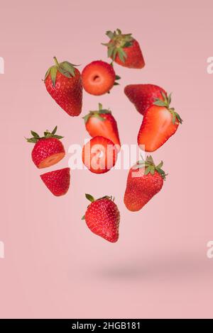 Composition créative avec fraises mûres volantes sur fond rose vif.Vitamines, concept d'aliments frais et sains.Idée de fruit minimale.Paille en tranches Banque D'Images