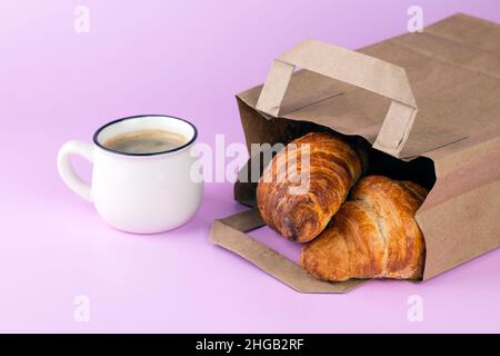 Tasse de café et croissants dans un sac en papier sur fond rose pastel.Concept de livraison alimentaire et d'emballage écologique. Banque D'Images