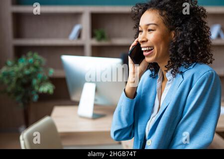 Belle femme d'affaires adulte avec une robe élégante debout dans un studio d'affaires et utilisant une application de téléphone mobile - African american portrait femme dans un bus Banque D'Images