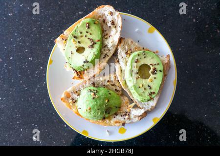 Tranches d'avocat sur des tranches de pain rustiques avec des graines de sésame noir et des flocons de piment placés sur une assiette vue de dessus en bas Banque D'Images