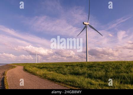 Route sur la côte près de la mer et moulin électrique vent. Le fond est un ciel bleu agréable avec des nuages blancs dans le temps ensoleillé.Il y a de l'herbe verte autour. Banque D'Images