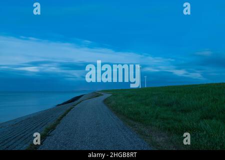 Route autour de la mer et éoliennes sur une pelouse verte.Photo au coucher du soleil.Il y a de beaux nuages bleus dans le ciel. Banque D'Images