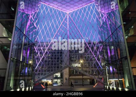 L'atrium du 55 Baker Street, Londres, présente des lumières violettes entre les panneaux de verre et semble impressionnant au crépuscule lorsque les piétons et les bus passent Banque D'Images