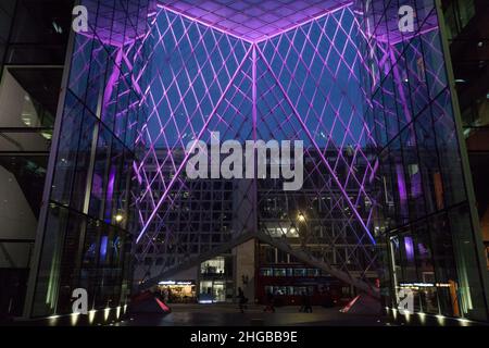 L'atrium du 55 Baker Street, Londres, présente des lumières violettes entre les panneaux de verre et semble impressionnant au crépuscule lorsque les piétons et les bus passent Banque D'Images