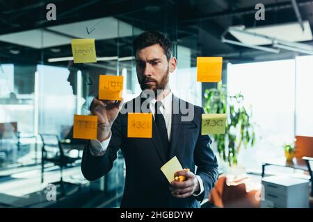 homme d'affaires en réflexion sur un plan de travail en verre, porte des plans sur des autocollants en papier de couleur, des plans pour un avenir proche Banque D'Images
